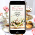 Animated storybook tea party digital invitation displayed on a phone, featuring a watercolor tea set and flowers rising from an open book in a whimsical garden scene.