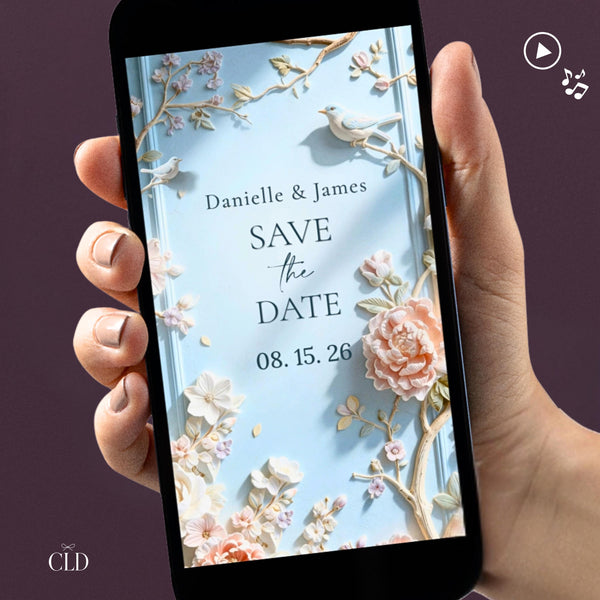 Animated save the date video evite shown on a phone screen, featuring sculpted bas relief florals in powder blue with peonies, cherry blossoms and birds, names and wedding date displayed in soft serif typography, against an aubergine background.